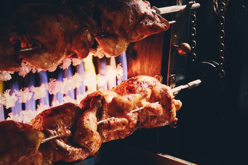 Rotisserie chickens roasting over blue flames